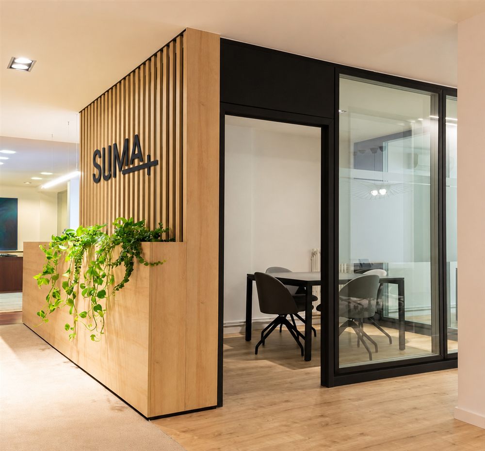 Entrada de las oficinas de Suma Canales de Venta con el logo SUMA+ en madera, símbolo de una intermediación energética que da la cara